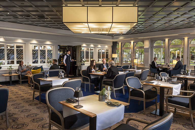 Elegantes Restaurant mit Gästen, die speisen und entspannen. Moderne Einrichtung und große Fenster mit Ausblick.