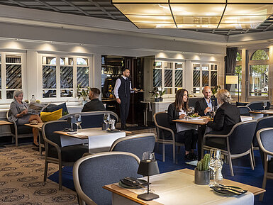 Elegantes Restaurant mit Gästen, die speisen und entspannen. Moderne Einrichtung und große Fenster mit Ausblick.