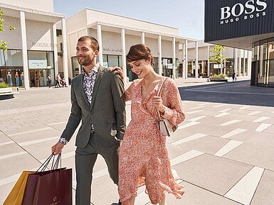 Paar beim Shopping in modernem Outlet Center mit Einkaufstüten und Markenstores