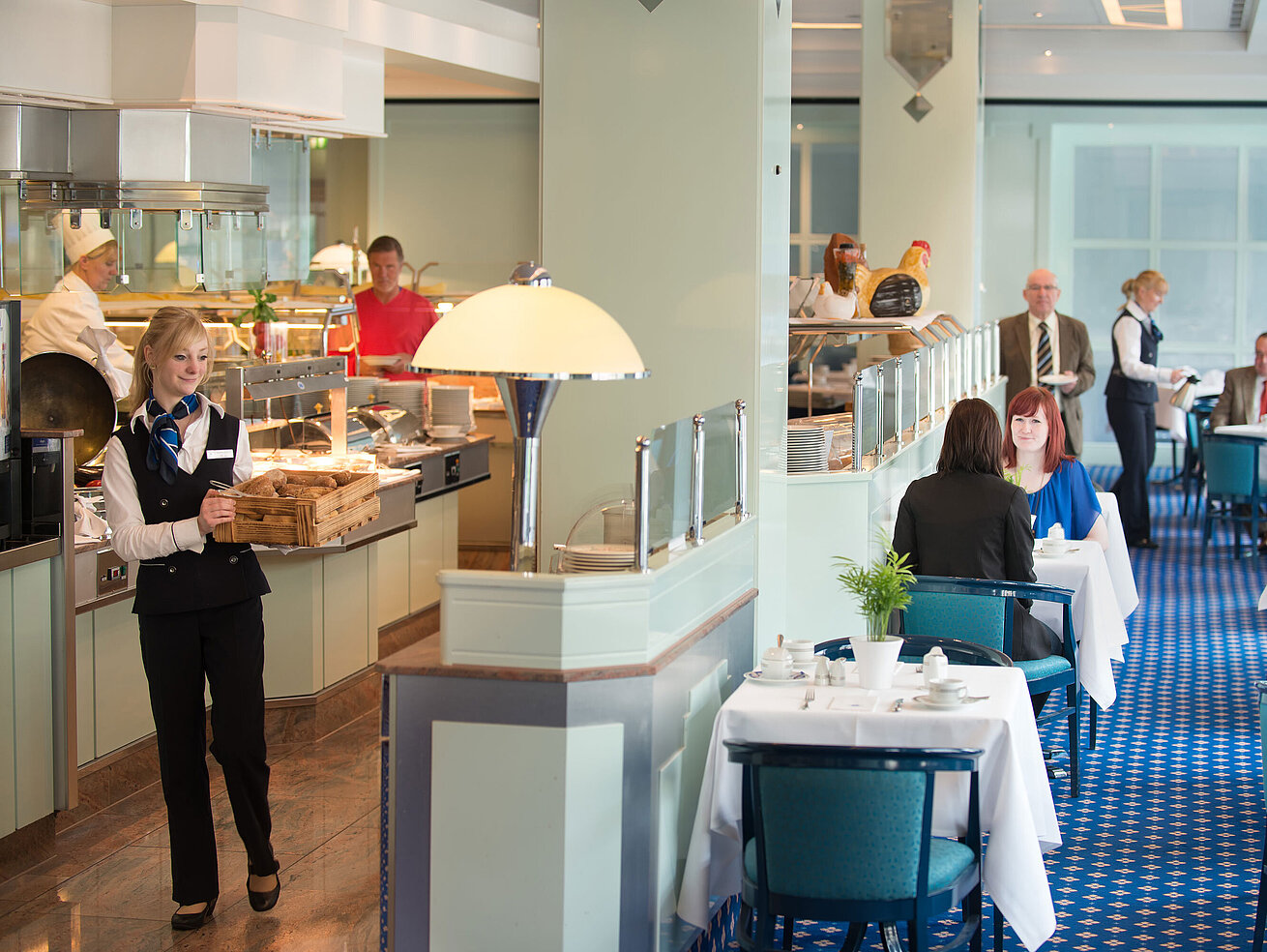 Eine Kellnerin bringt frische Brötchen zum Frühstücksbereich im Maritim Hotel Magdeburg, während Gäste am Tisch sitzen.