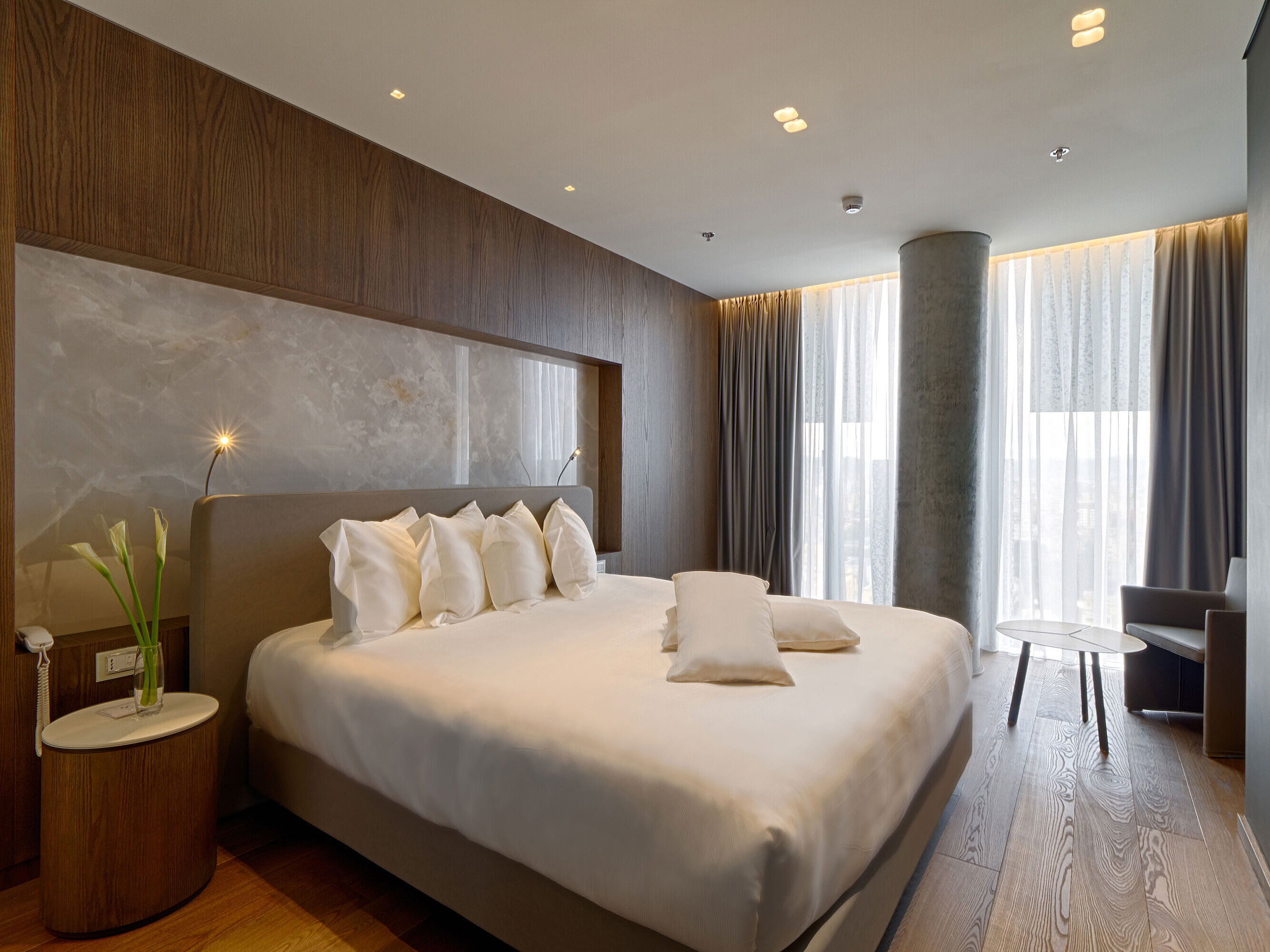 Ruhiges Zimmer mit großem Bett, Natursteinwand und weichen Vorhängen im Maritim Hotel Plaza Tirana