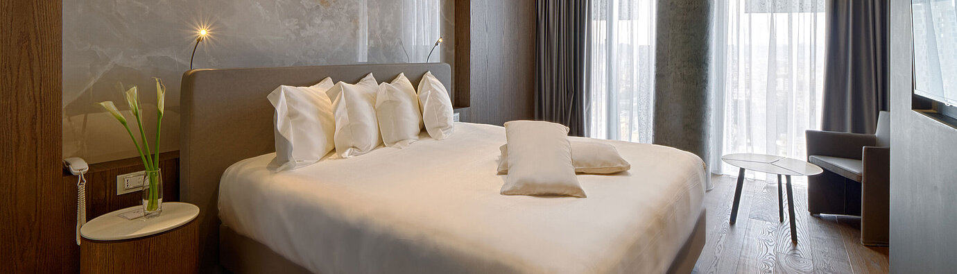 Ruhiges Zimmer mit großem Bett, Natursteinwand und weichen Vorhängen im Maritim Hotel Plaza Tirana