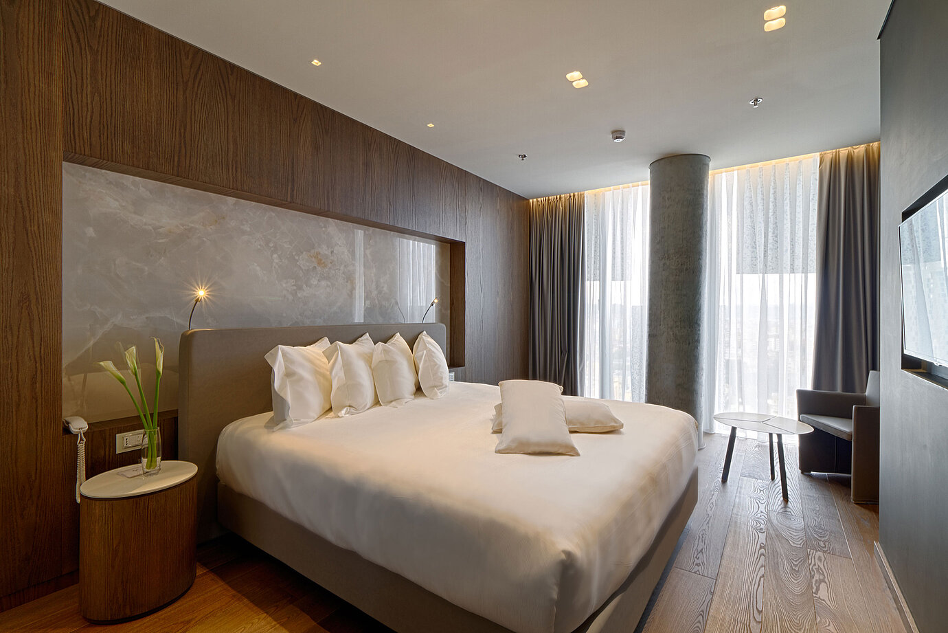 Ruhiges Zimmer mit großem Bett, Natursteinwand und weichen Vorhängen im Maritim Hotel Plaza Tirana
