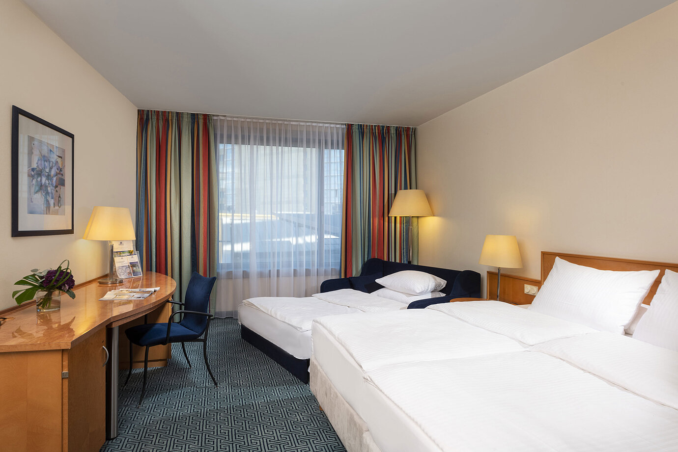 Classic Familienzimmer im Maritim Hotel Frankfurt mit Doppelbett, Schlafsofa, Schreibtisch und bunten Vorhängen.