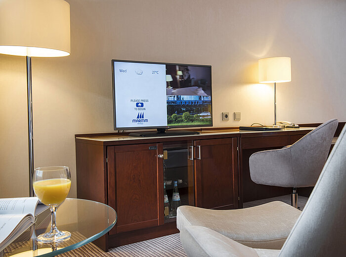 Detail eines Zimmers im Maritim Hotel Bonn mit Fernseher, Schreibtisch und Glas Orangensaft auf dem Tisch.