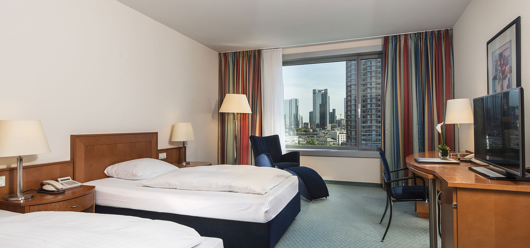 Comfort Zimmer im Maritim Hotel Frankfurt mit zwei Einzelbetten, Schreibtisch, Sitzbereich und Blick auf die Skyline.