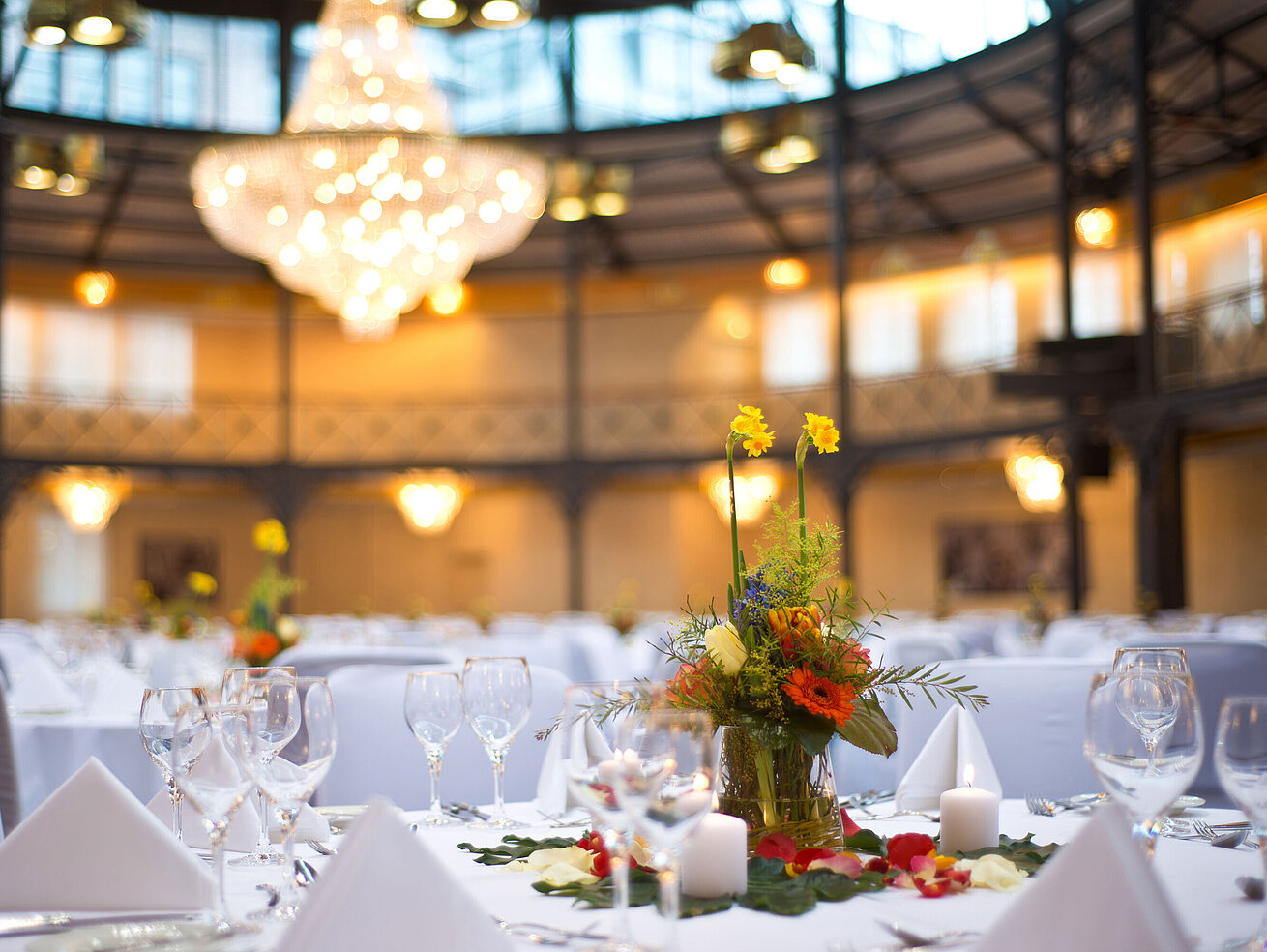 Detailansicht Tagungsraum Nahaufnahme einer Tischdekoration mit Blumen und Kerzen, im Hintergrund ein großer Kronleuchter