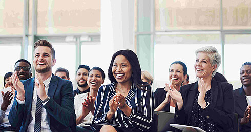 © Nicola – AdobeStock.com Teilnehmer applaudieren bei Konferenz oder Seminar im Tagungsraum