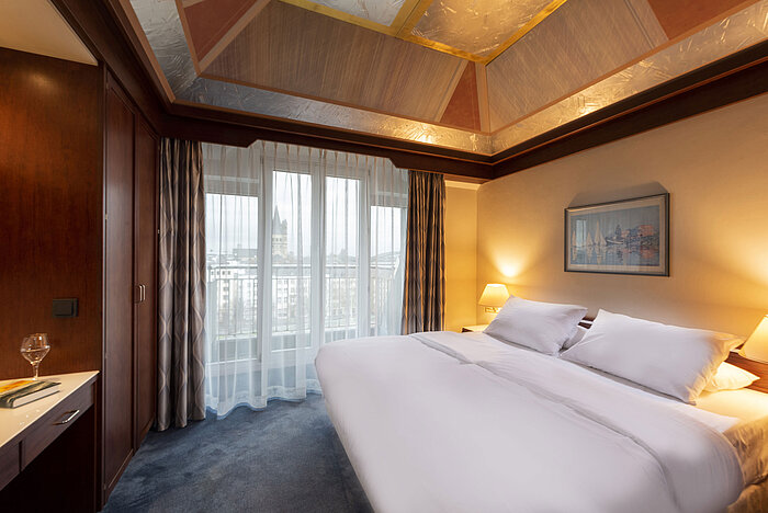 Junior Suite im Maritim Hotel Köln mit einem großen Bett, Schreibtisch, eleganter Decke und Panoramablick durch große Fenster