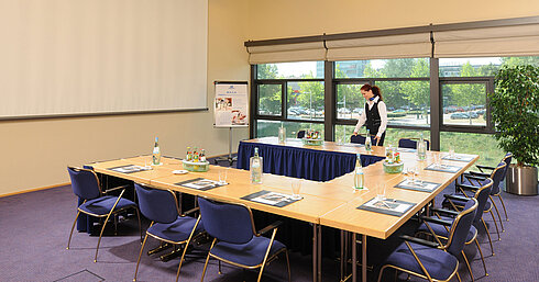 Tagungsraum im Maritim Hotel Dresden mit U-förmiger Tischanordnung, Präsentationsleinwand und Vorbereitungen für ein Meeting.