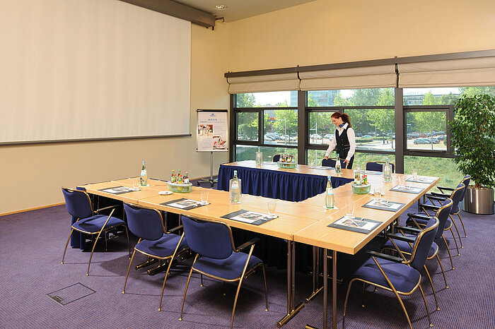 Tagungsraum im Maritim Hotel Dresden mit U-förmiger Tischanordnung, Präsentationsleinwand und Vorbereitungen für ein Meeting.