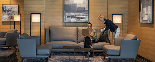 Zwei Frauen arbeiten in der eleganten Lounge des Maritim Hotel Ingolstadt mit Laptop und moderner Einrichtung.