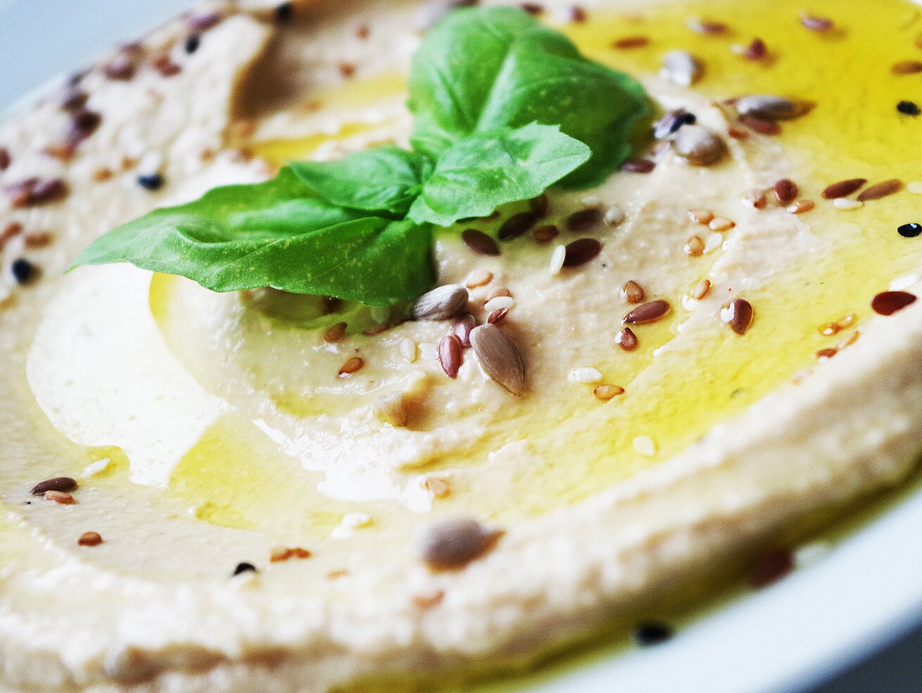 Cremiger Hummus mit Olivenöl, Kichererbsen und frischen Kräutern angerichtet.