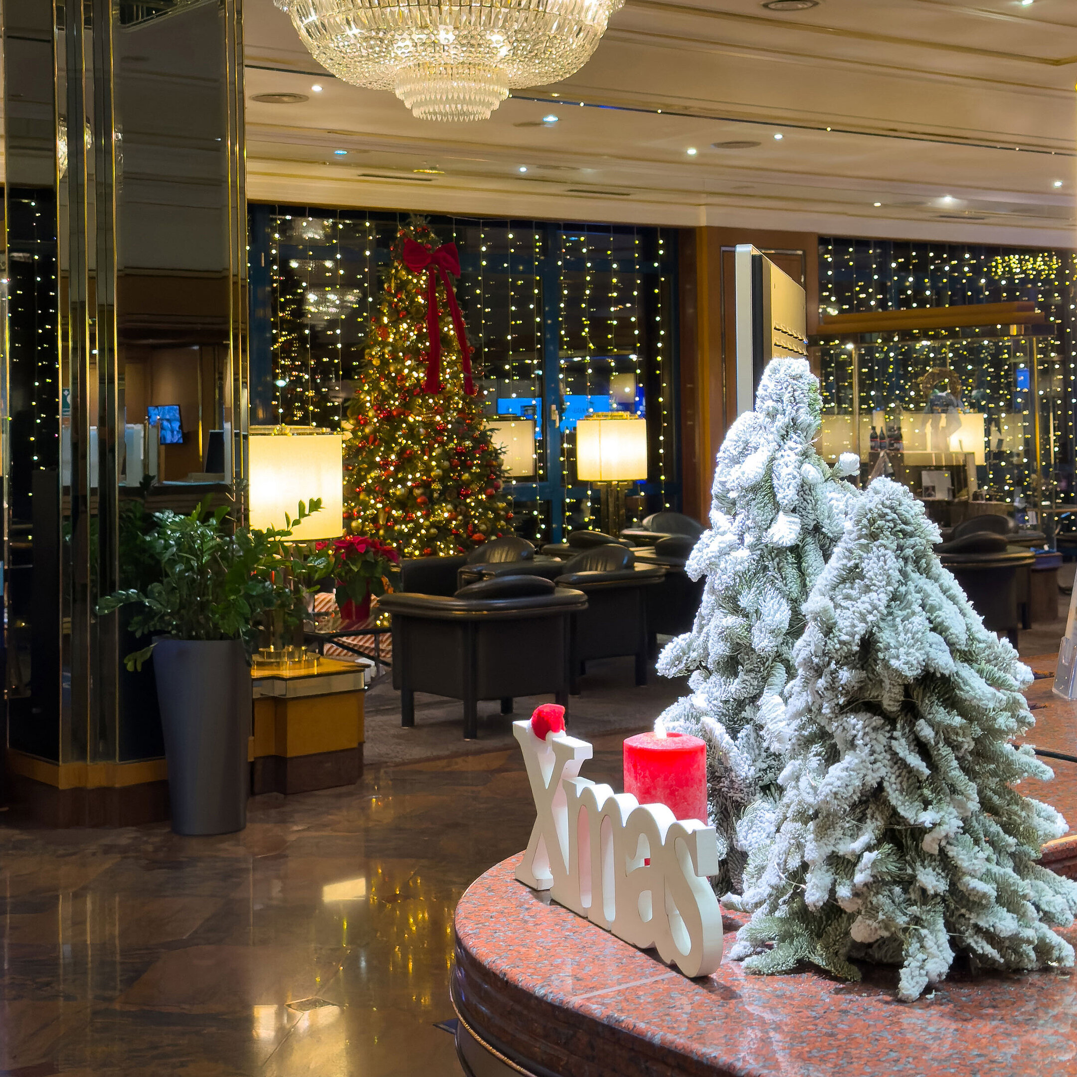 Festlich dekorierte Hotellobby mit geschmückten Weihnachtsbäumen, Kronleuchter und winterlicher Atmosphäre.