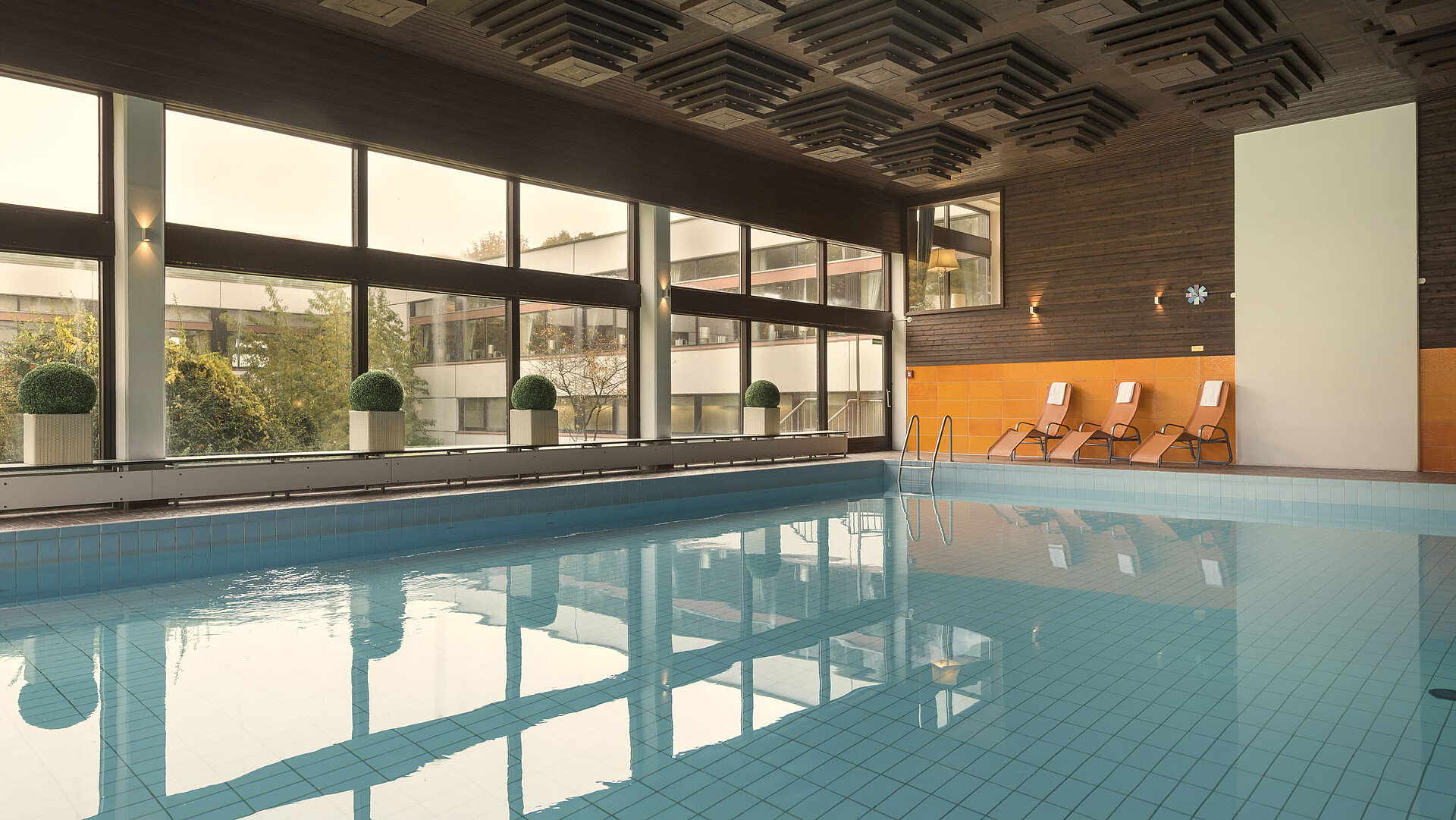 Schwimmbad Das Bild zeigt den Innenpool des Maritim Hotels Kiel, umgeben von großen Fenstern, mit Liegestühlen für Entspannung.