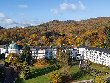 Außenansicht des Maritim Hotel Bad Wildungen, umgeben von Park, Bäumen und herbstlichem Waldpanorama.