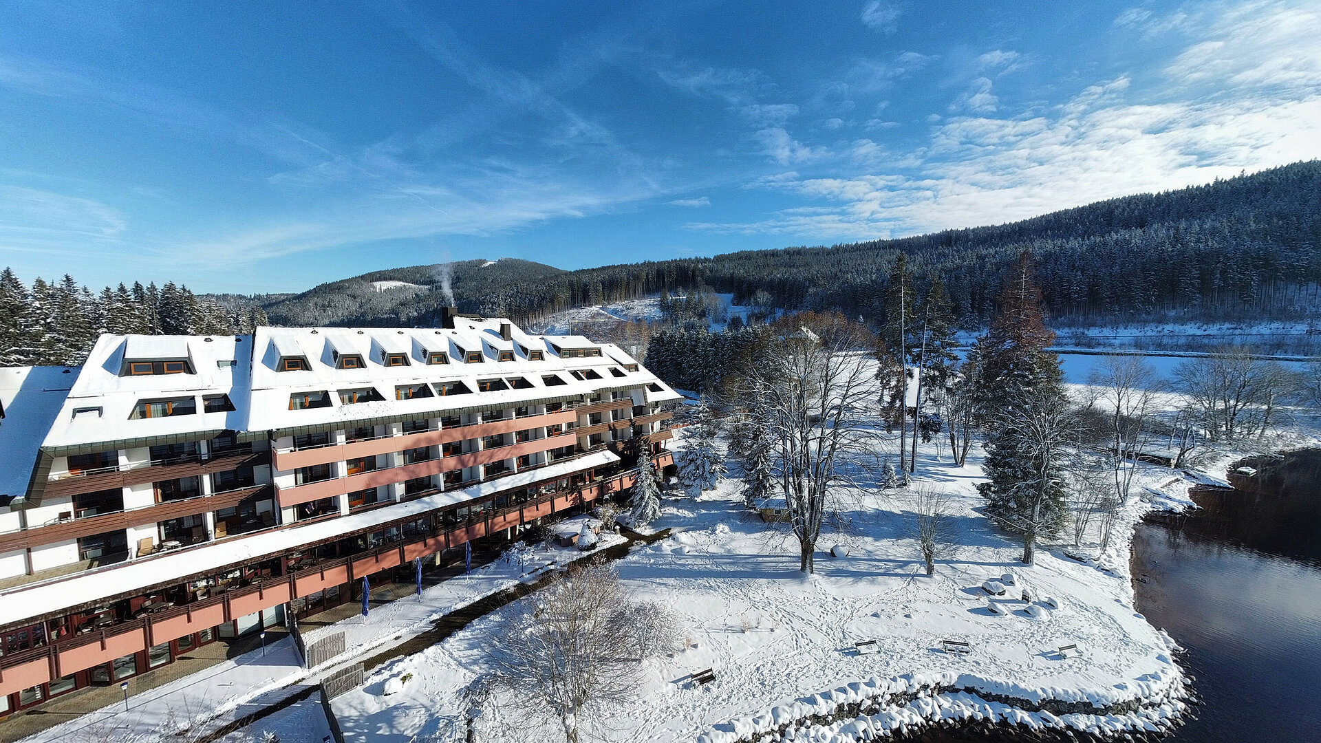 Maritim Hotel Titisee im Winter mit verschneitem Garten und Blick auf das Hotelgebäude am Ufer