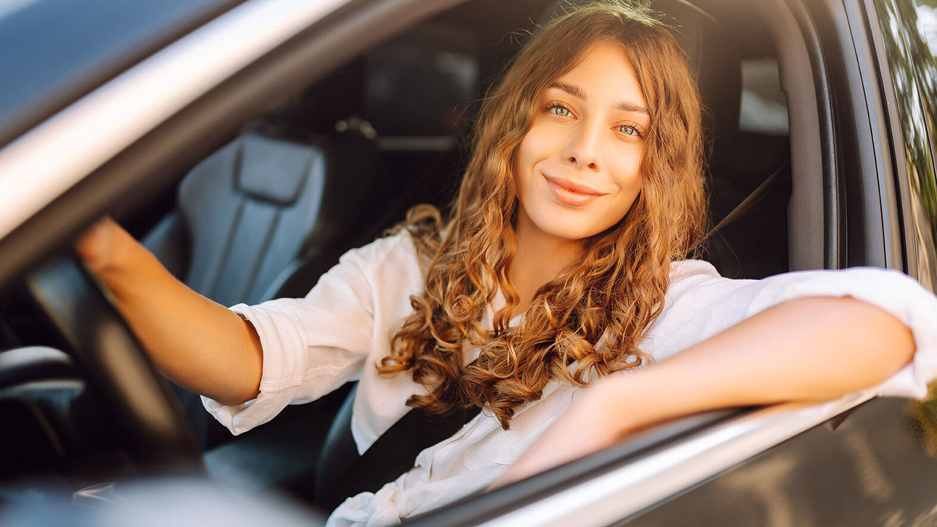 Junge Frau sitzt lächelnd am Steuer eines Autos und genießt die Fahrt