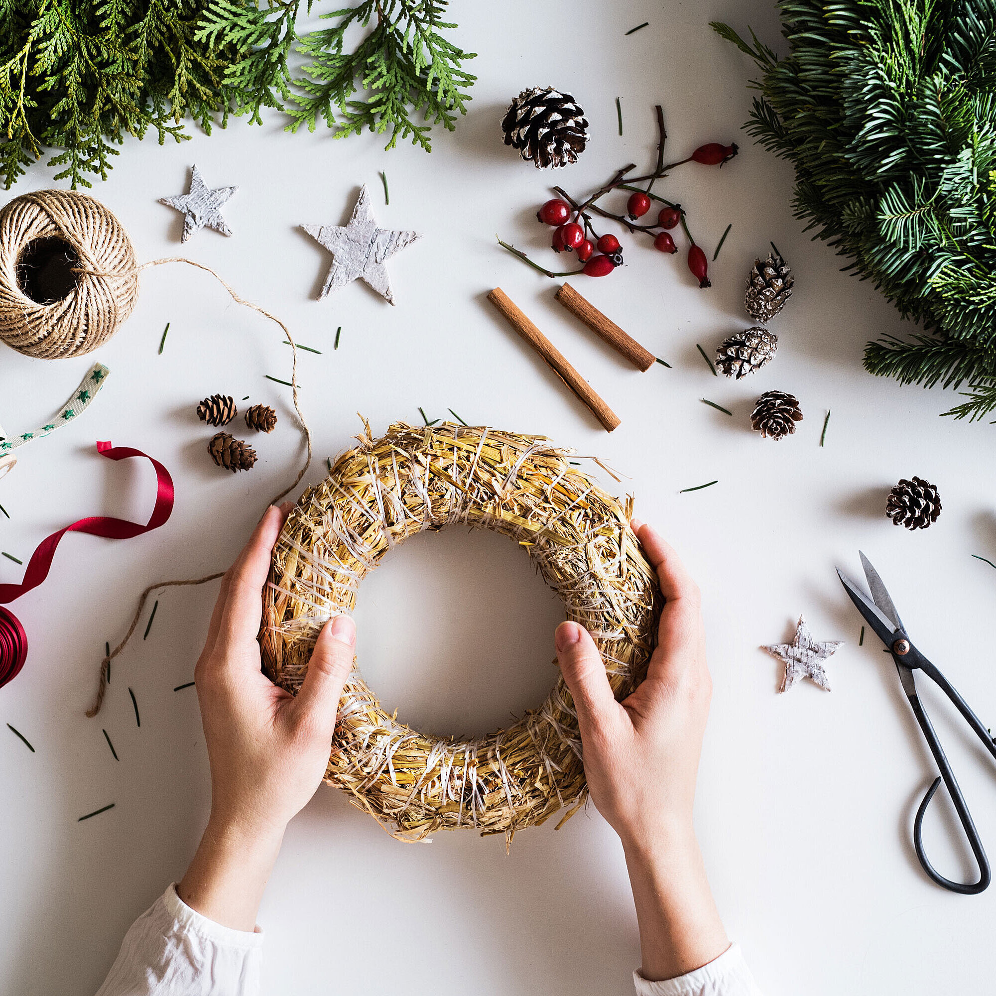 Adventskranz gestalten © Halfpoint - AdobeStock.com Hände gestalten einen Adventskranz auf einem Tisch mit Tannenzweigen, Schleifen und Bastelmaterial.