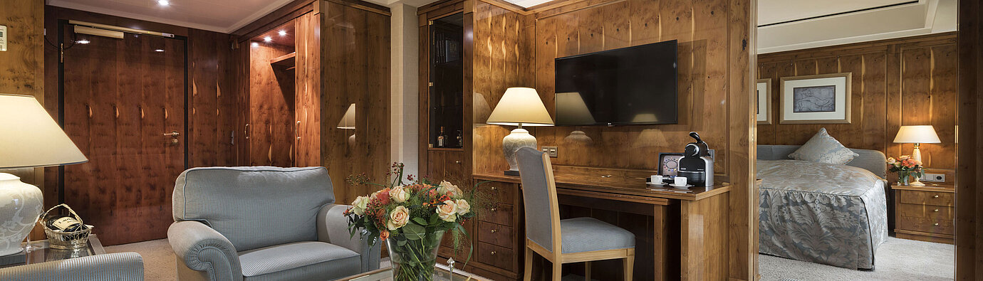 Penthouse-Suite mit Wohnzimmer, Holzmöbeln, Schreibtisch und Blick ins Schlafzimmer im Maritim Seehotel Timmendorfer Strand.
