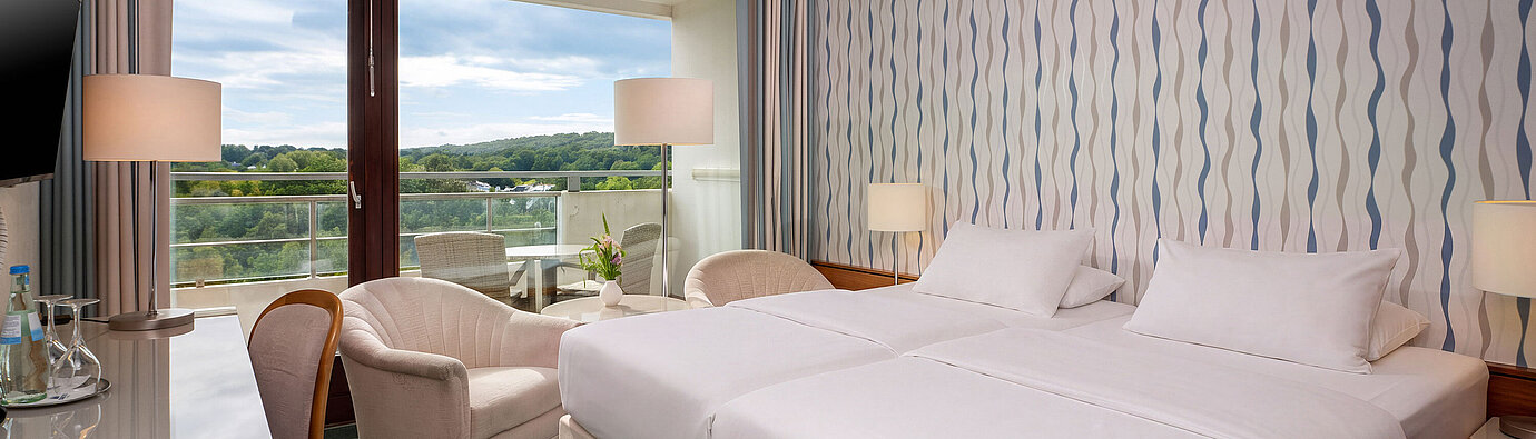 Classic Zimmer mit Doppelbett, Schreibtisch, Sessel und großem Fenster mit Blick ins Grüne