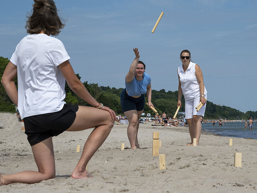 Drei Personen spielen Wikingerschach am Strand vor dem Maritim Seehotel Timmendorfer Strand bei sonnigem Wetter.