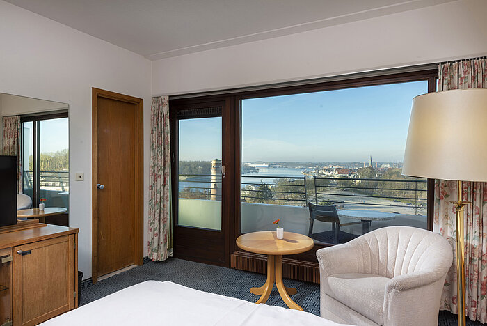 Helles Hotelzimmer mit Balkon, Schreibtisch und Ausblick auf die Trave und die Lübecker Bucht