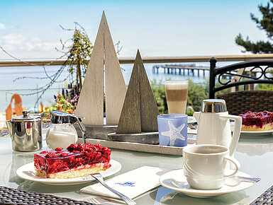 Kaffeetafel mit Kuchen und Heißgetränken auf der Terrasse des Maritim Seehotel Timmendorfer Strand mit Meerblick.