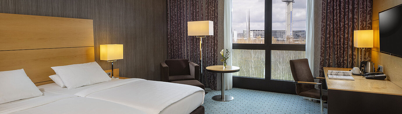 Classic Zimmer im Maritim Hotel Düsseldorf mit Doppelbett, Schreibtisch und Panoramafenster mit Blick auf die Umgebung.