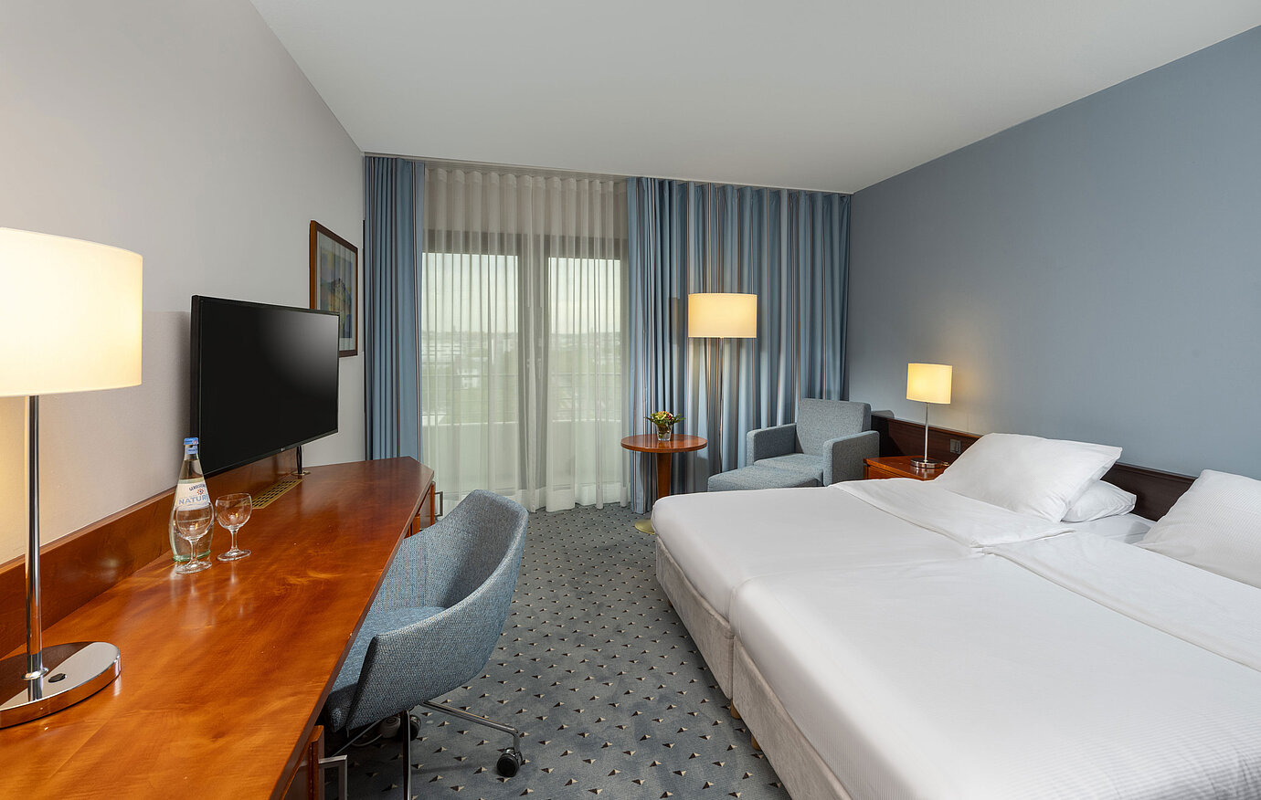 Classic Doppelzimmer im Maritim Darmstadt mit Schreibtisch, Flachbildfernseher, Sitzecke und großen Fenstern mit Vorhängen.