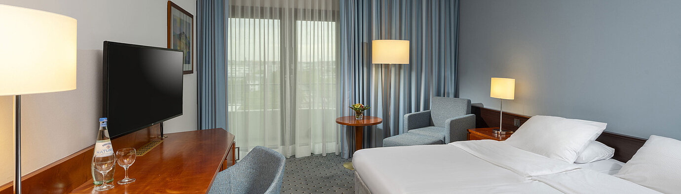 Classic Doppelzimmer im Maritim Darmstadt mit Schreibtisch, Flachbildfernseher, Sitzecke und großen Fenstern mit Vorhängen.