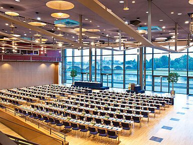 Großer Konferenzsaal im Maritim Hotel Dresden mit Reihen blauer Stühle und Blick auf die Elbe.