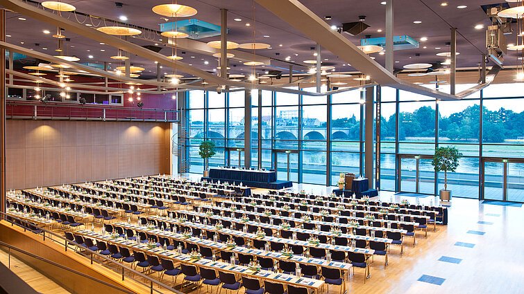Großer Konferenzsaal im Maritim Hotel Dresden mit Reihen blauer Stühle und Blick auf die Elbe.