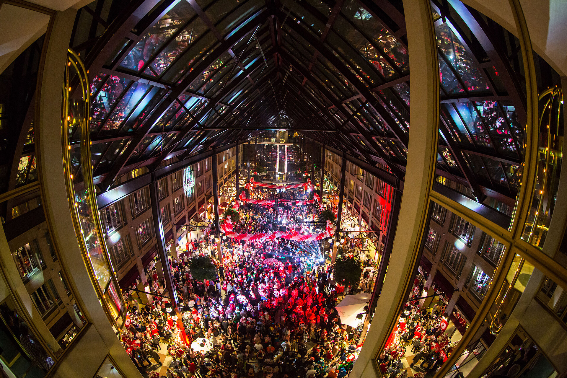 Karneval im Maritim Hotel Köln, große Menschenmenge in der festlich dekorierten Lobby mit bunten Lichtern und Kostümen.
