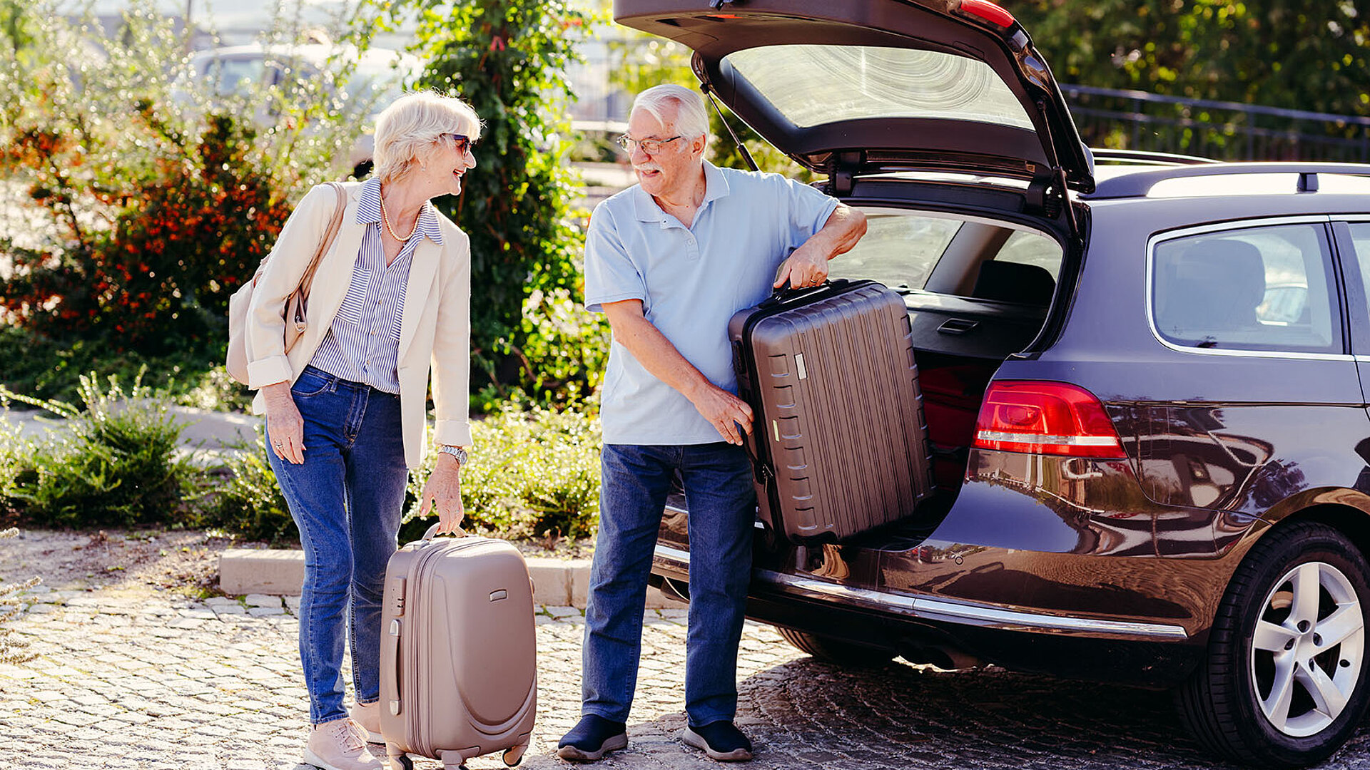 Älteres Paar lädt Koffer aus dem Kofferraum eines Autos und bereitet sich auf eine Reise vor.