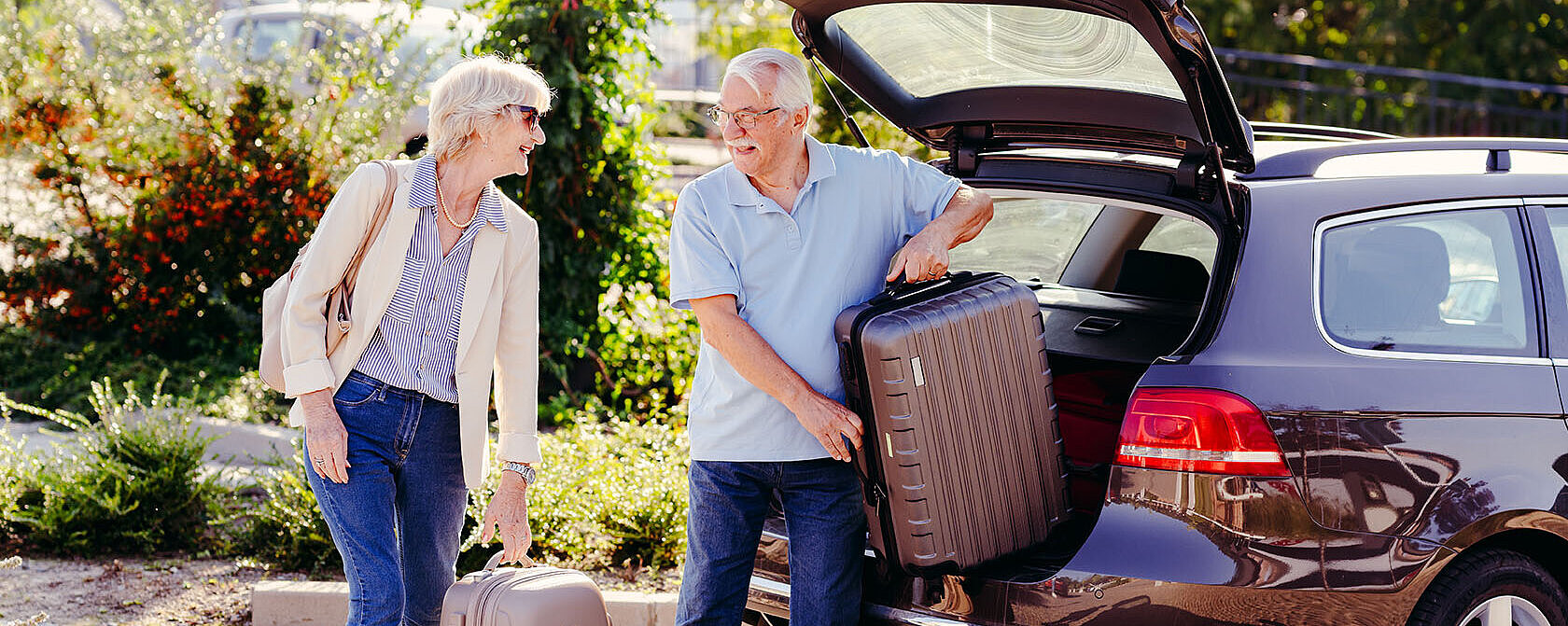 © lordn Älteres Paar lädt Koffer aus dem Kofferraum eines Autos und bereitet sich auf eine Reise vor.