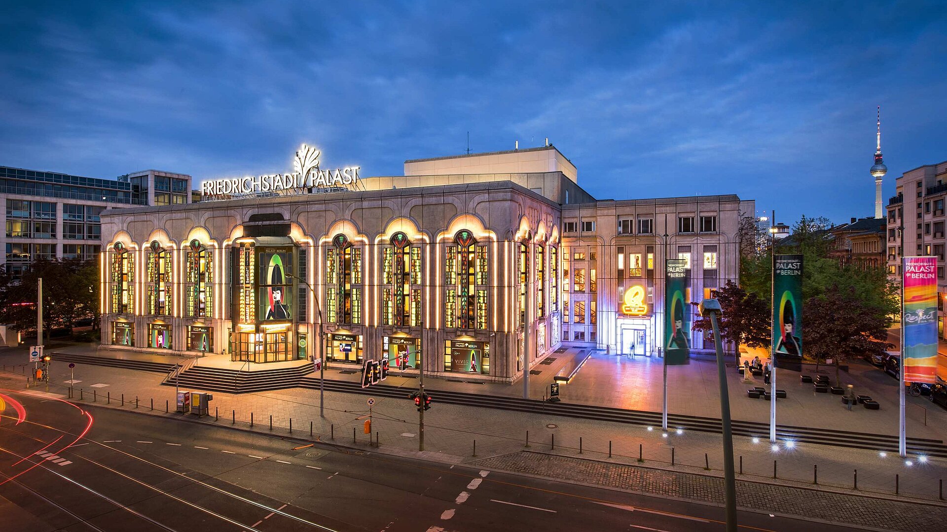 Beleuchteter Friedrichstadt-Palast in Berlin bei Abenddämmerung mit Fernsehturm im Hintergrund