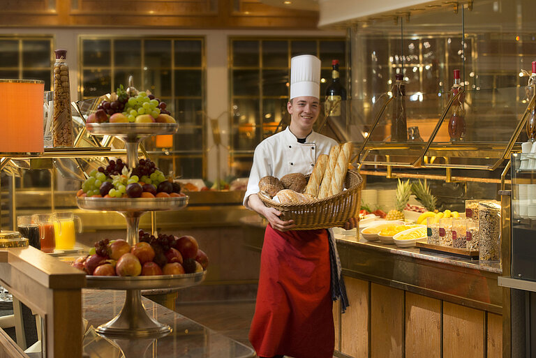 Bäcker mit Brotkorb am Frühstücksbuffet des Maritim Hotel Stuttgart, umgeben von frischem Obst