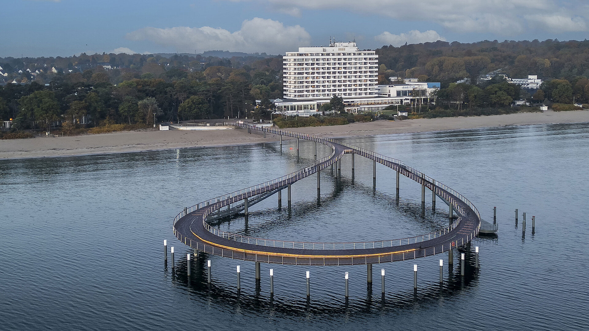 Seebrücke vor dem Maritim Seehotel Timmendorfer Strand mit ruhigem Wasser und blauem Himmel.