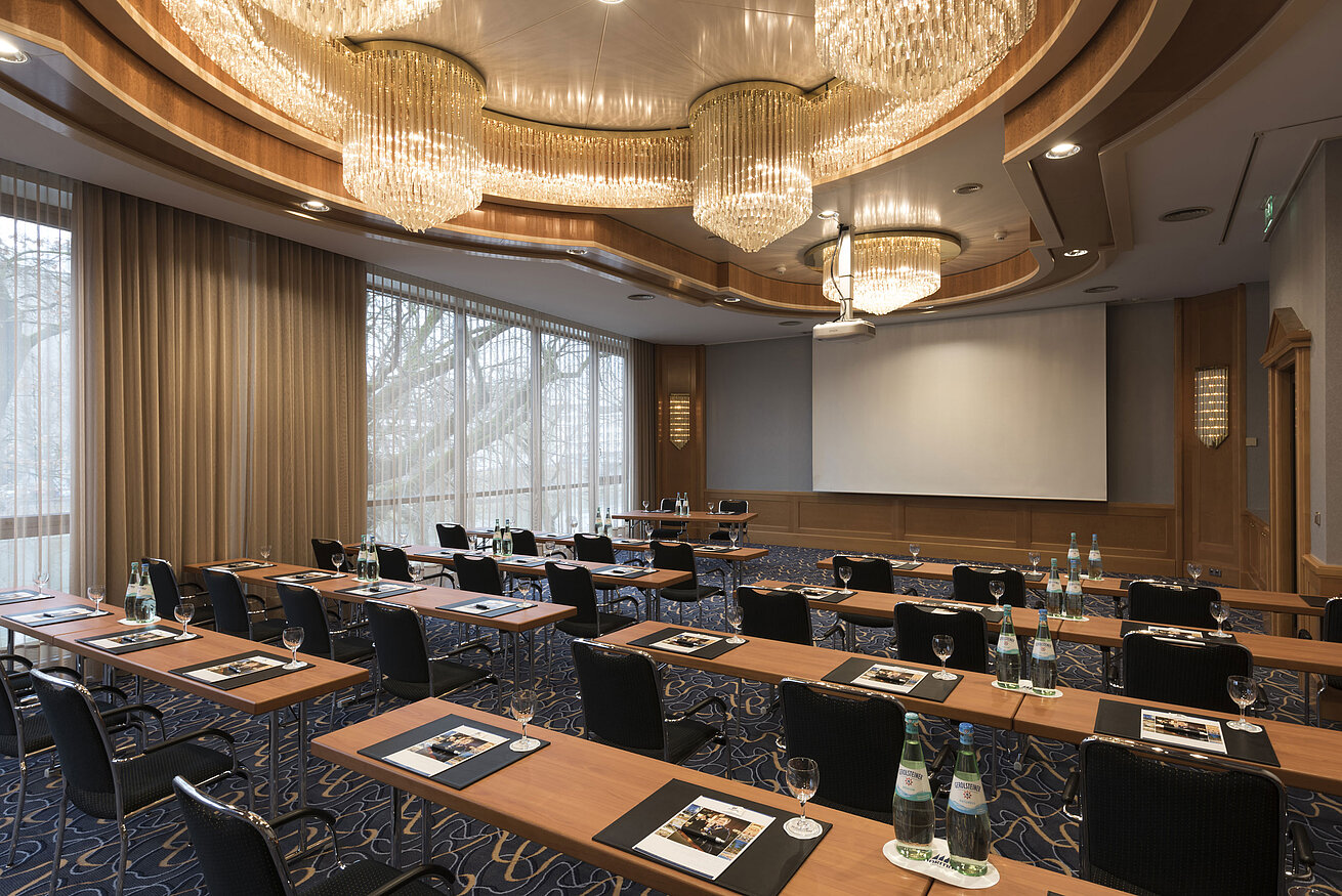 Eleganter Tagungsraum mit Reihenbestuhlung, Kronleuchtern und Projektionsfläche im Maritim Hotel Ulm.