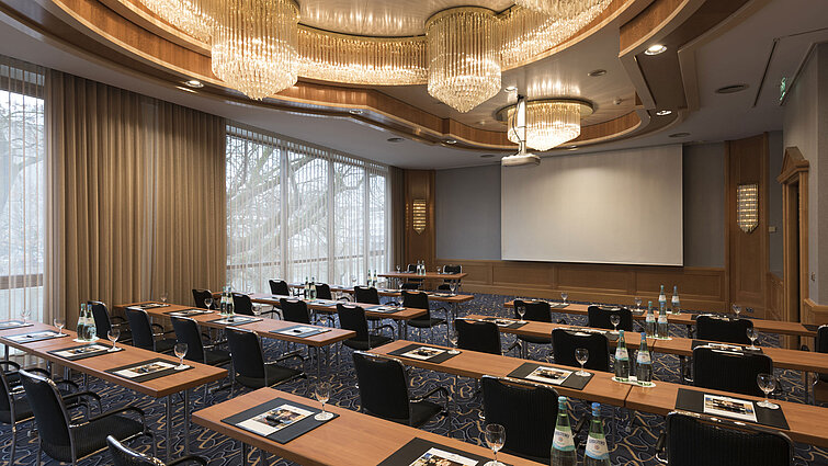 Eleganter Tagungsraum mit Reihenbestuhlung, Kronleuchtern und Projektionsfläche im Maritim Hotel Ulm.