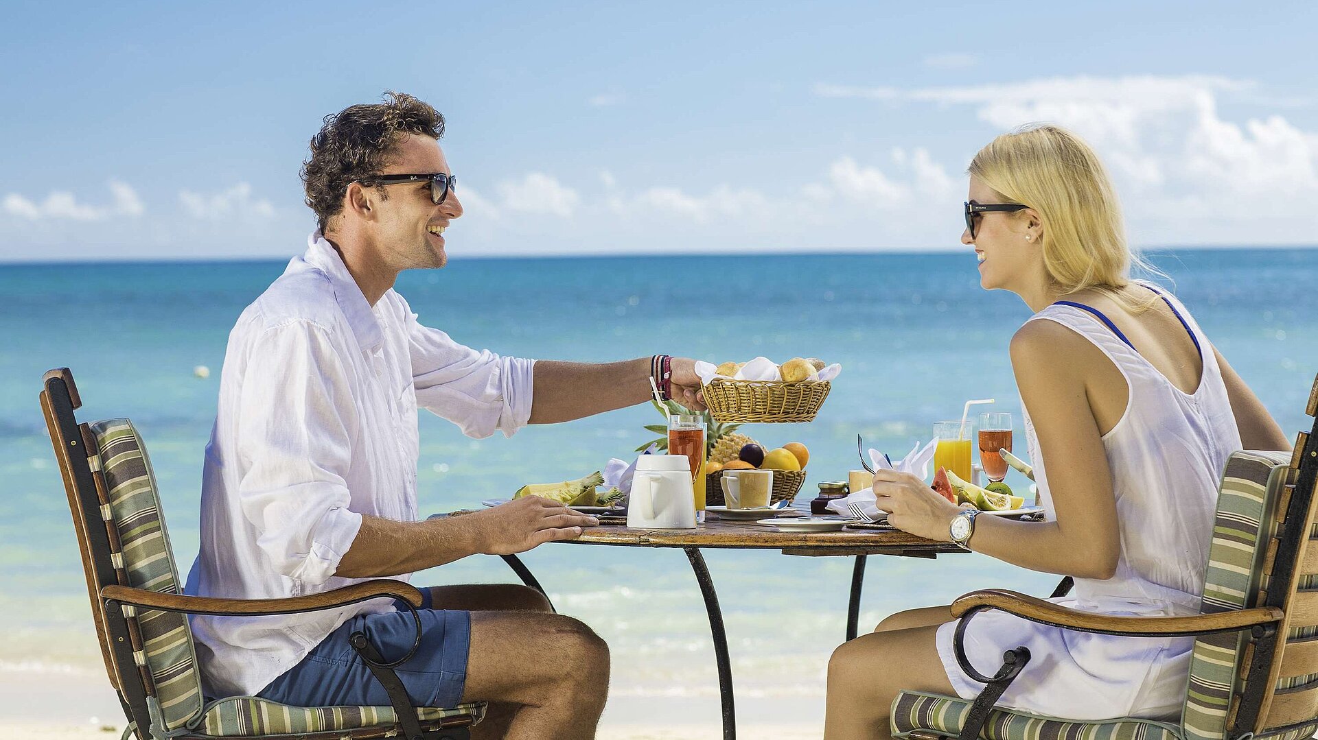Paar genießt entspanntes Frühstück am Strand mit Meerblick an einem sonnigen Urlaubstag