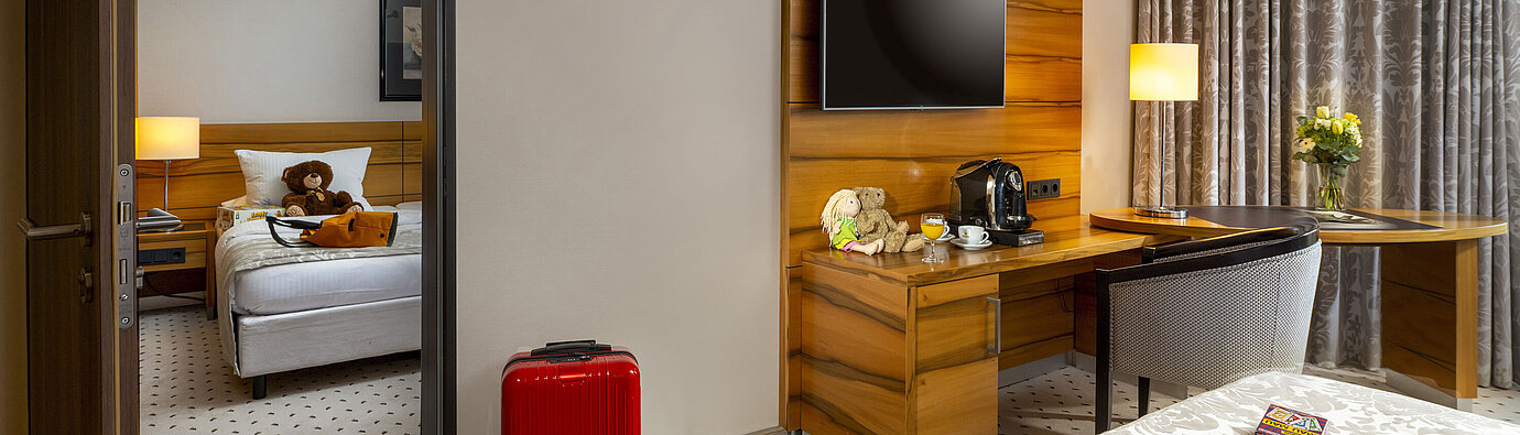 Familienzimmer im Maritim Hotel Bad Homburg mit separatem Kinderzimmer, rotem Koffer und Kuscheltier.