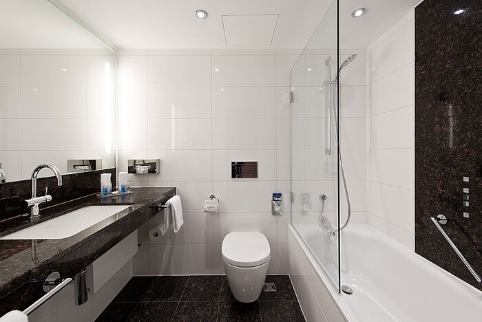 Modernes Badezimmer im Maritim Hotel Darmstadt mit eleganter Badewanne, dunkler Granit-Arbeitsplatte und heller Wandgestaltung.