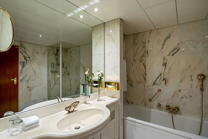 Modernes Badezimmer im Maritim Hotel Hannover mit Badewanne, Glasdusche und Marmorwänden.