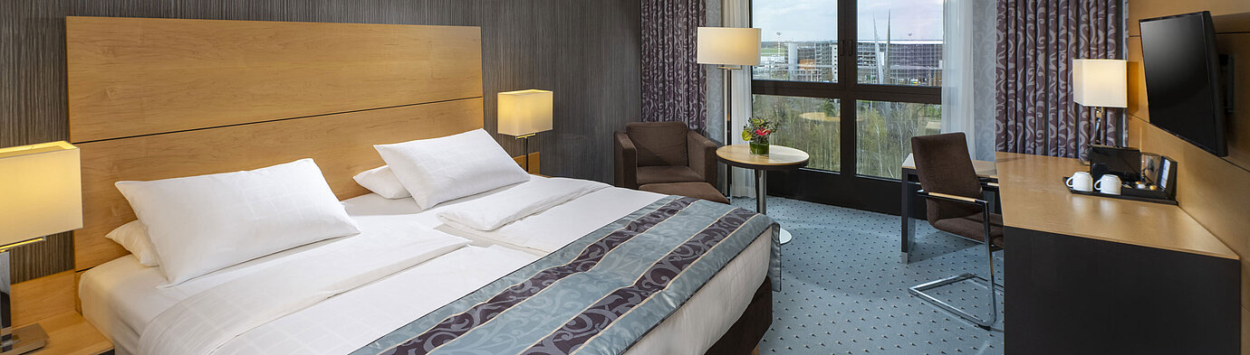 Modernes Superior-Zimmer im Maritim Hotel Düsseldorf mit großem Bett, Schreibtisch und Blick auf die Stadt.