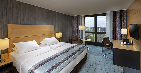 Modernes Superior-Zimmer im Maritim Hotel Düsseldorf mit großem Bett, Schreibtisch und Blick auf die Stadt.