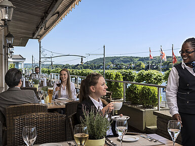Gäste genießen Kaffee und Wein auf der Terrasse des Maritim Hotel Königswinter mit malerischem Blick auf den Rhein.