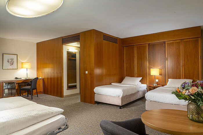 Helles Familienzimmer mit drei Betten, Schreibtisch und stilvoller Holzverkleidung im Maritim Hotel Stuttgart