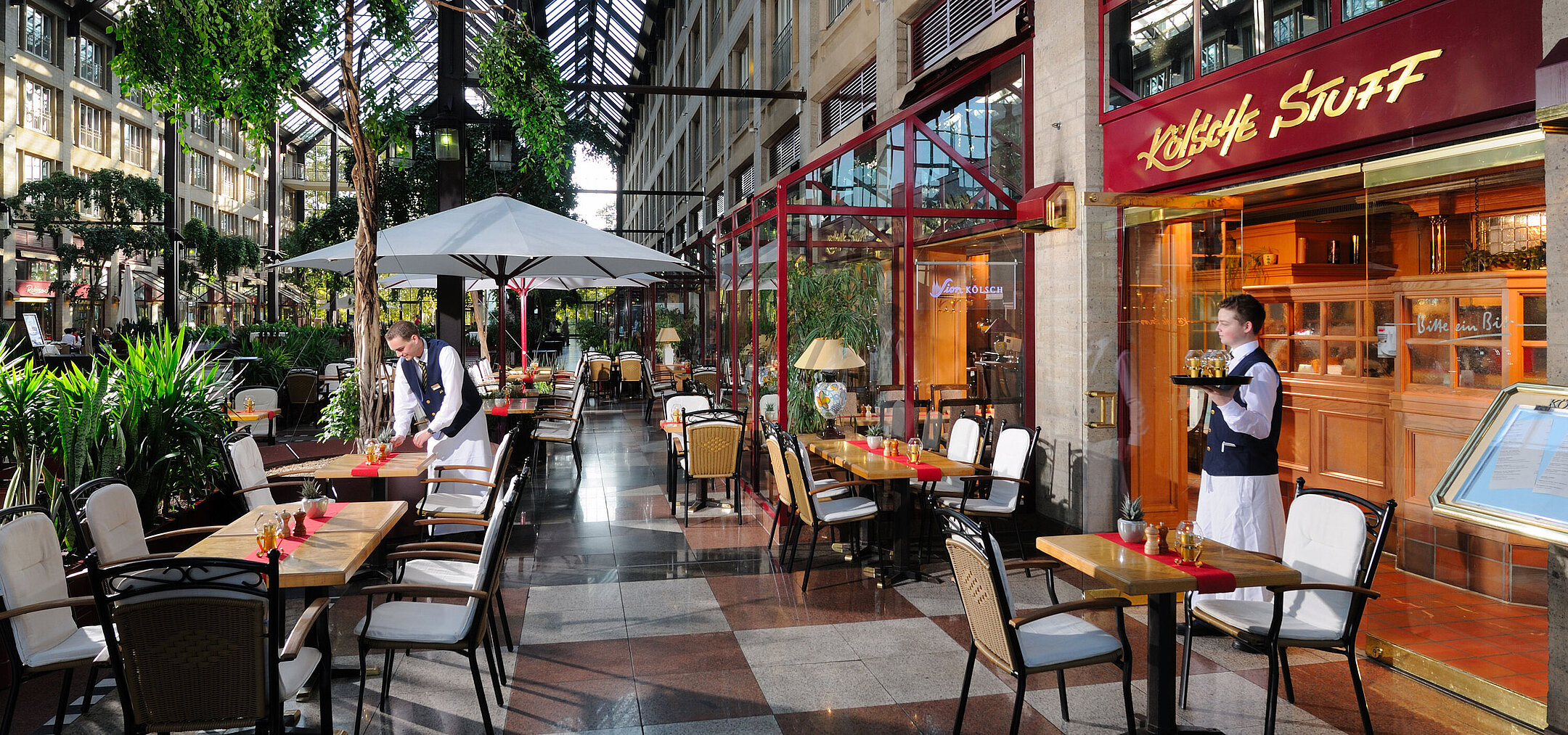 Restaurant Kölsche Stuff im Maritim Hotel Köln, gemütliche Einrichtung mit Bedienung und Außensitzbereich unter Glasdach.